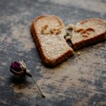 dry rose flower next to broken heart shaped cookie