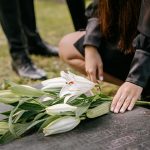 woman in black clothes holding white flowers on grave